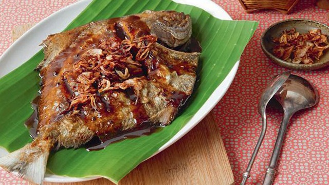 fried and glazed pompano fish on plate with a banana leaf