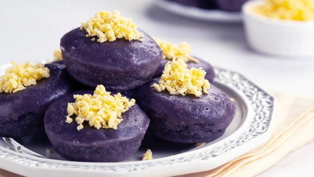 stack of ube puto topped with grated cheese on an intricate plate