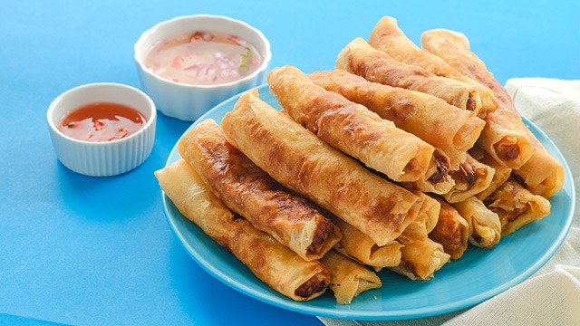 lumpiang shanghai stacked high on a blue plate, with a side of ketchup and spiced vinegar