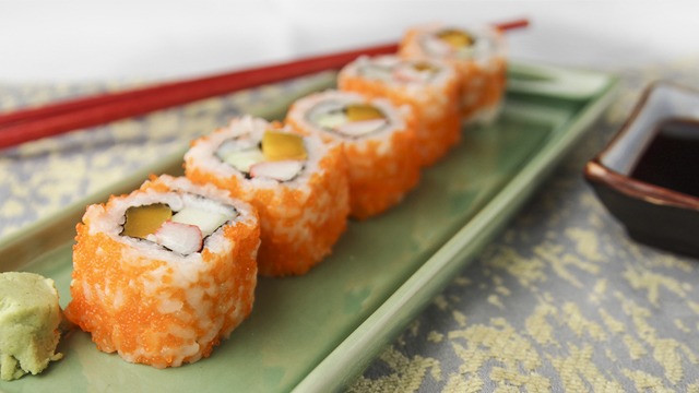 A serving of wasabi and a row of california maki on a rectangular sushi plate. Beside the plate is a pair of chopsticks and a dipping bowl of soy sauce.