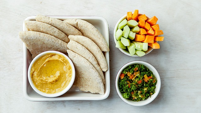 bowl with hummus and pita bread with carrots and greens on the side