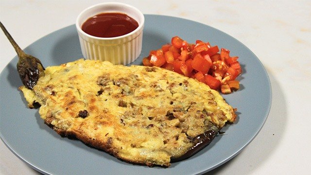 tortang talong on a blue plate with chopped tomatoes and ketchup