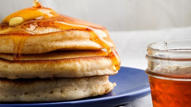stacked pancakes being topped with syrup