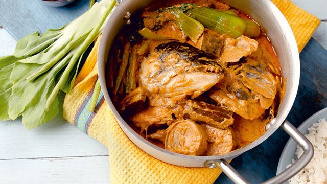 salmon head kare-kare in a big stock pot with a small container of bagoong on the side