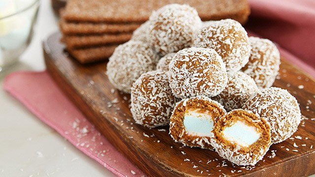 graham balls filled with cream cheese and covered in coconut shavings on wooden tray