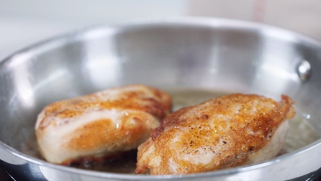 pork chops searing in a stainless steel pan