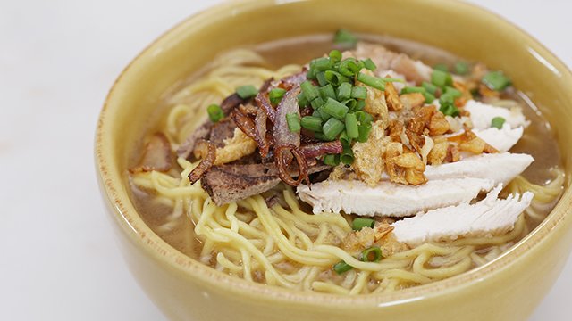la paz batchoy in a mustard colored bowl, topped with toasted shalltos, cgarlic, chicken and pork bits