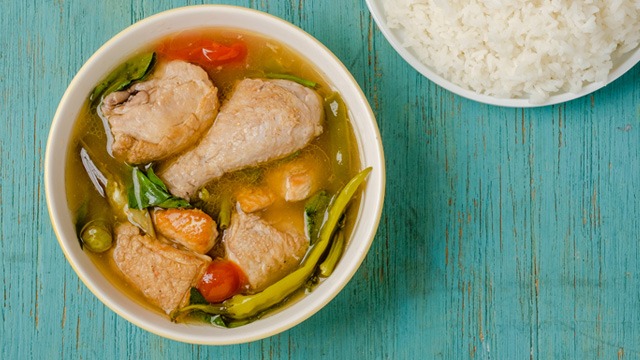 chicken sinigang with green chili, tomato, okra, and kangkong in a white serving bowl and rice on the side