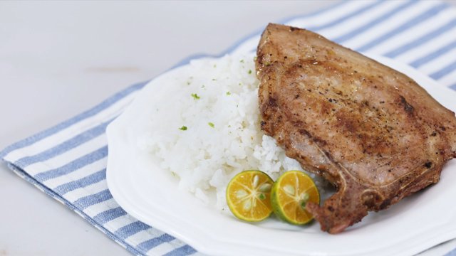 Fried calamansi pork chop on rice and calamansi on a white plate