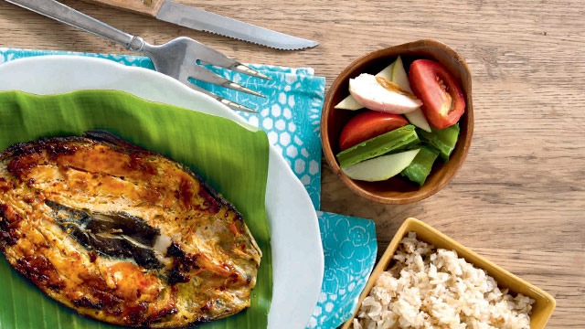 Bangus inasal on a banana leaf on a plate, with veggies and reice on the side