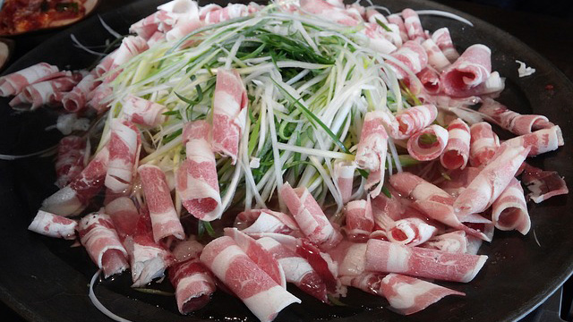 thinly sliced raw rolled pork on a grill, topped with fresh thinly sliced sprin onions