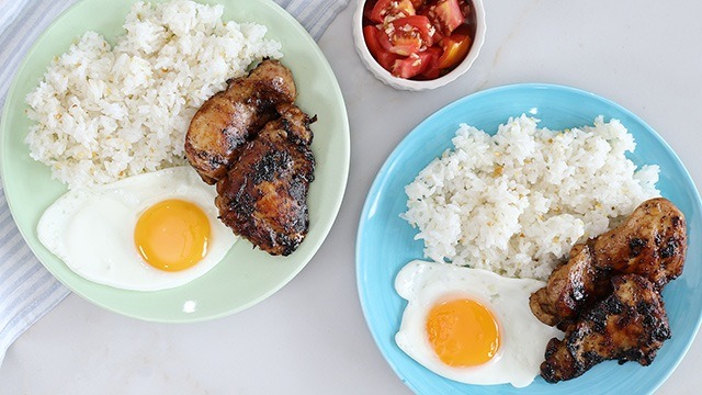 two plates of tocilog (tocino, sinangag, and itlog) on a green plate and a blue plate with tomatoes in a condiment dish