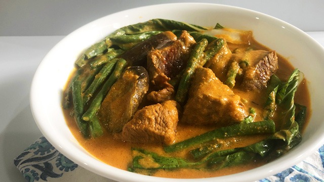beef kare-kare with bok choy and sitaw in a white bowl
