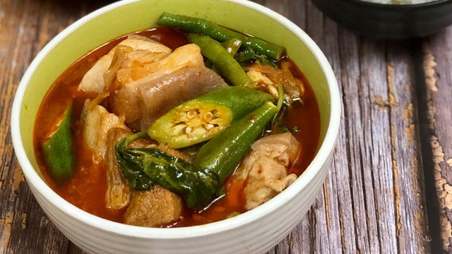 pork sinigang with kimchi, okra, kangkong in a white ceramic bowl