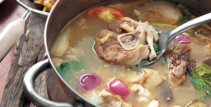 sinigang na baboy in a big steel pot, with a piece of pork getting scooped out