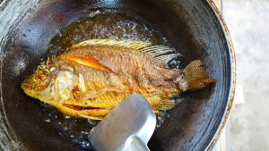 frying fish in oil in a wok with metal spatula