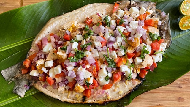 grilled bangus on a bed of banana leaves, topped with tomato and onions