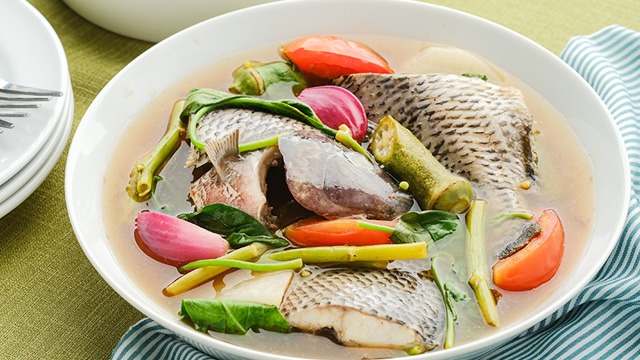 tilapia sinigang with okra, kangkong, tomatoes and onion in a big shallow white bowl