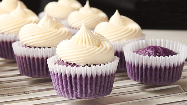 ube cupcakes with coconut frosting in white liners on cooling rack