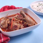 chicken callos in a rectangular bowl and rice in the background