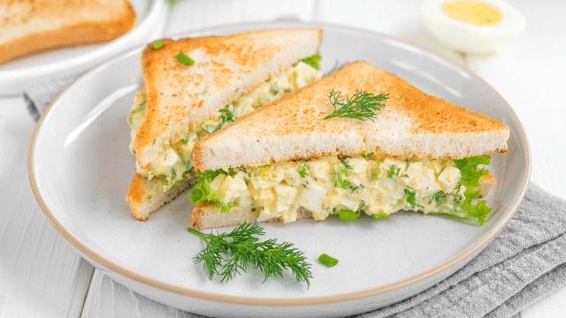 egg salad sandwich with toasted bread and lettuce on a white wooden background