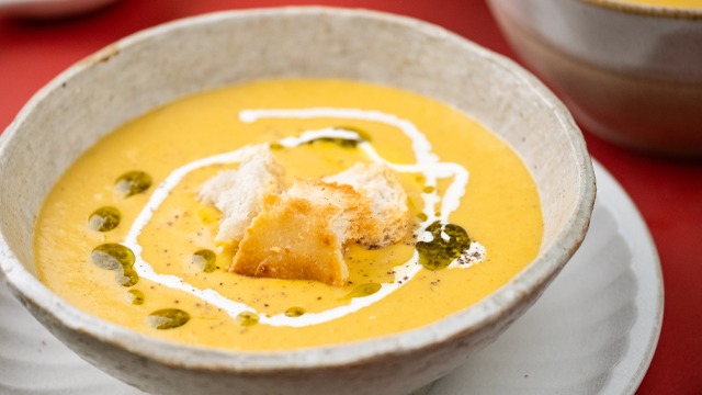 cream of kalabasa soup in a bowl with croutons pesto and cream