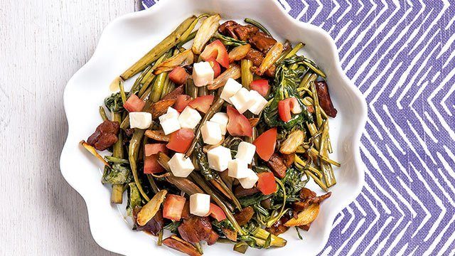adobong kangkong topped with feta cheese on a wavy plate