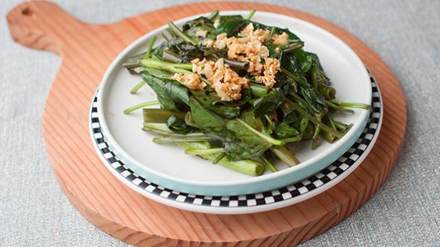 kangkongoystersauce-645 kangkong in oyster sauce in a shallow plate that's on a round wooden board